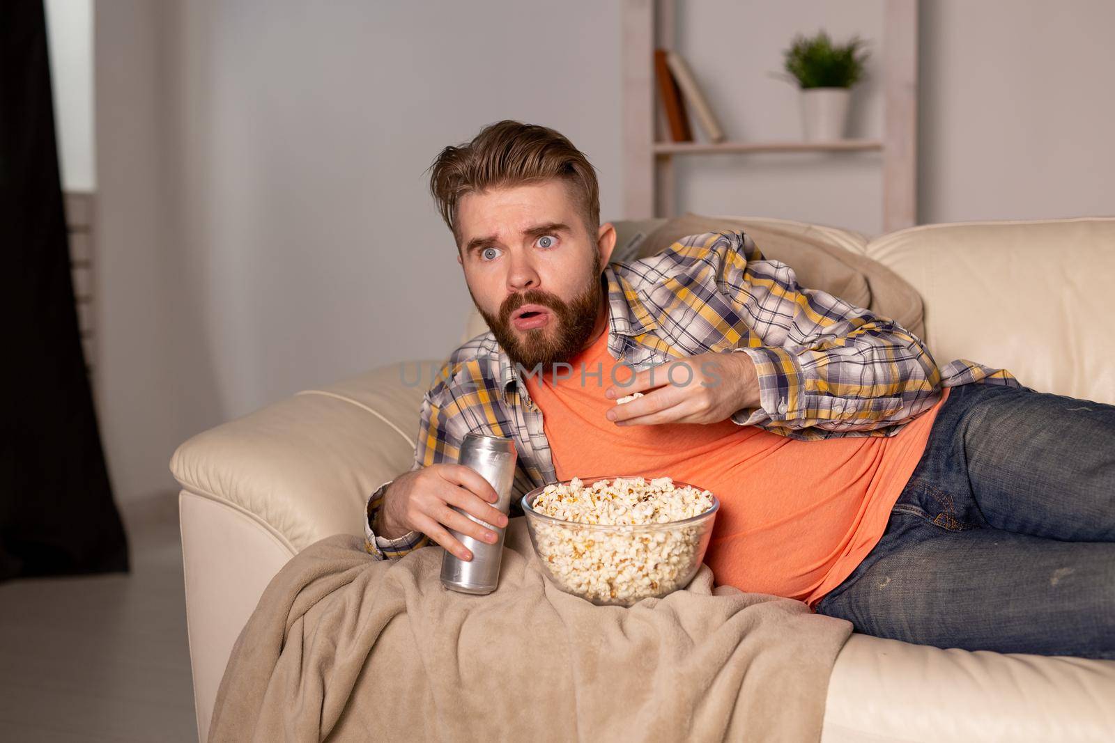 Bearded man watching film or sport games TV eating popcorn in house at night. Cinema, championship and fan.