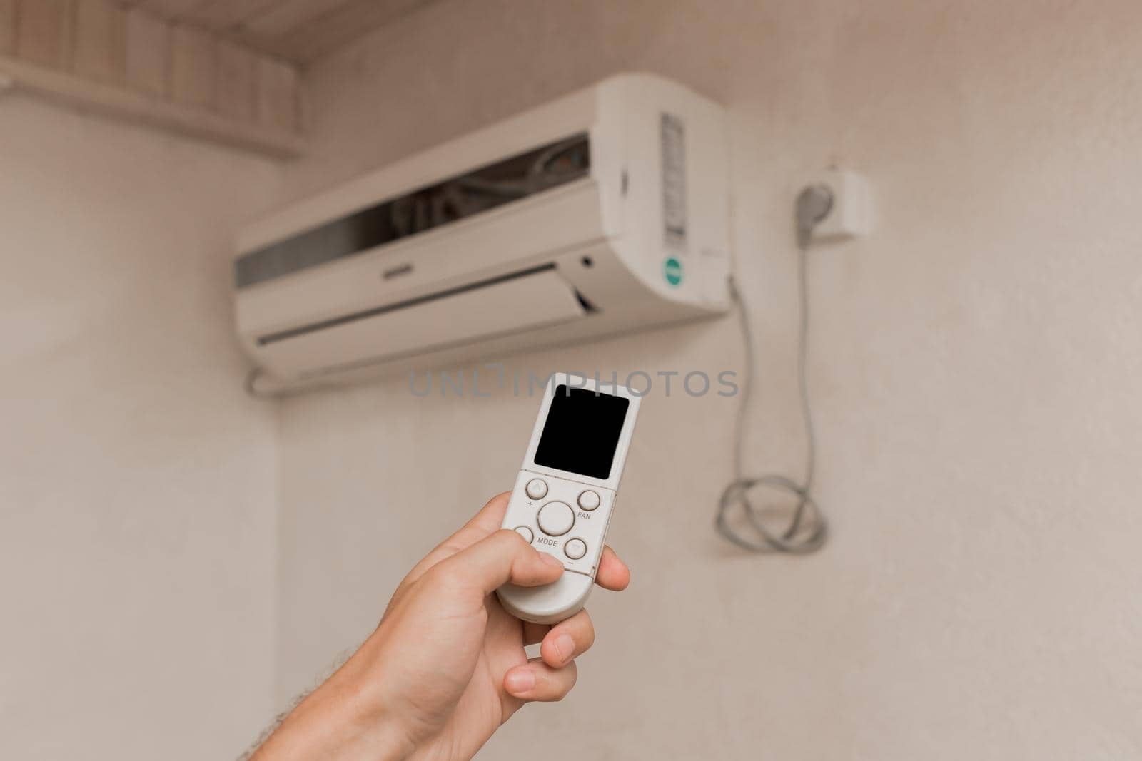 The guy's hand holds the remote control of the air conditioner. Cooling and temperature control in the room of the house by AYDO8