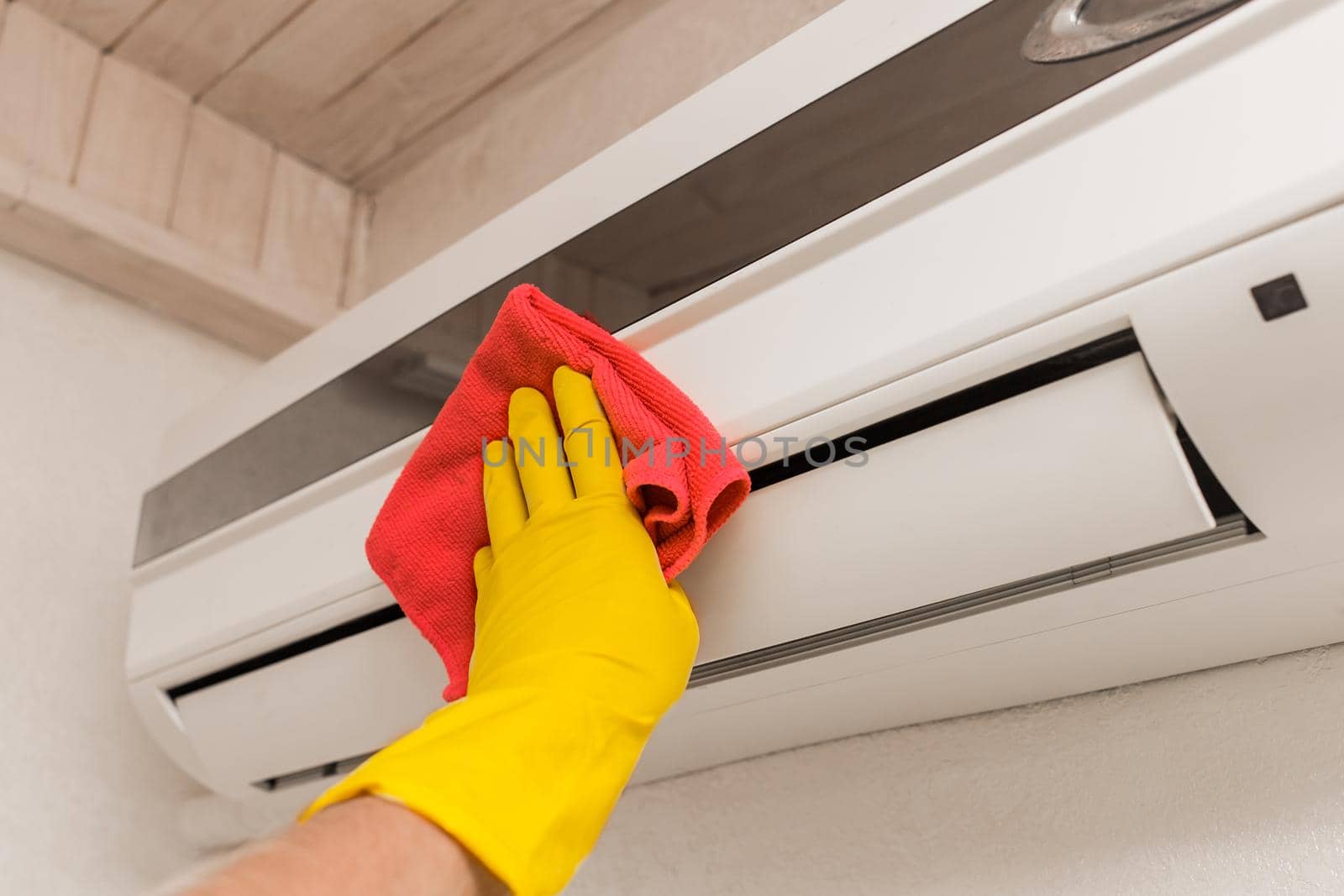 The hand of a man in a red household glove wipes and cleans the air conditioner. Maintenance and cleaning indoor service by AYDO8