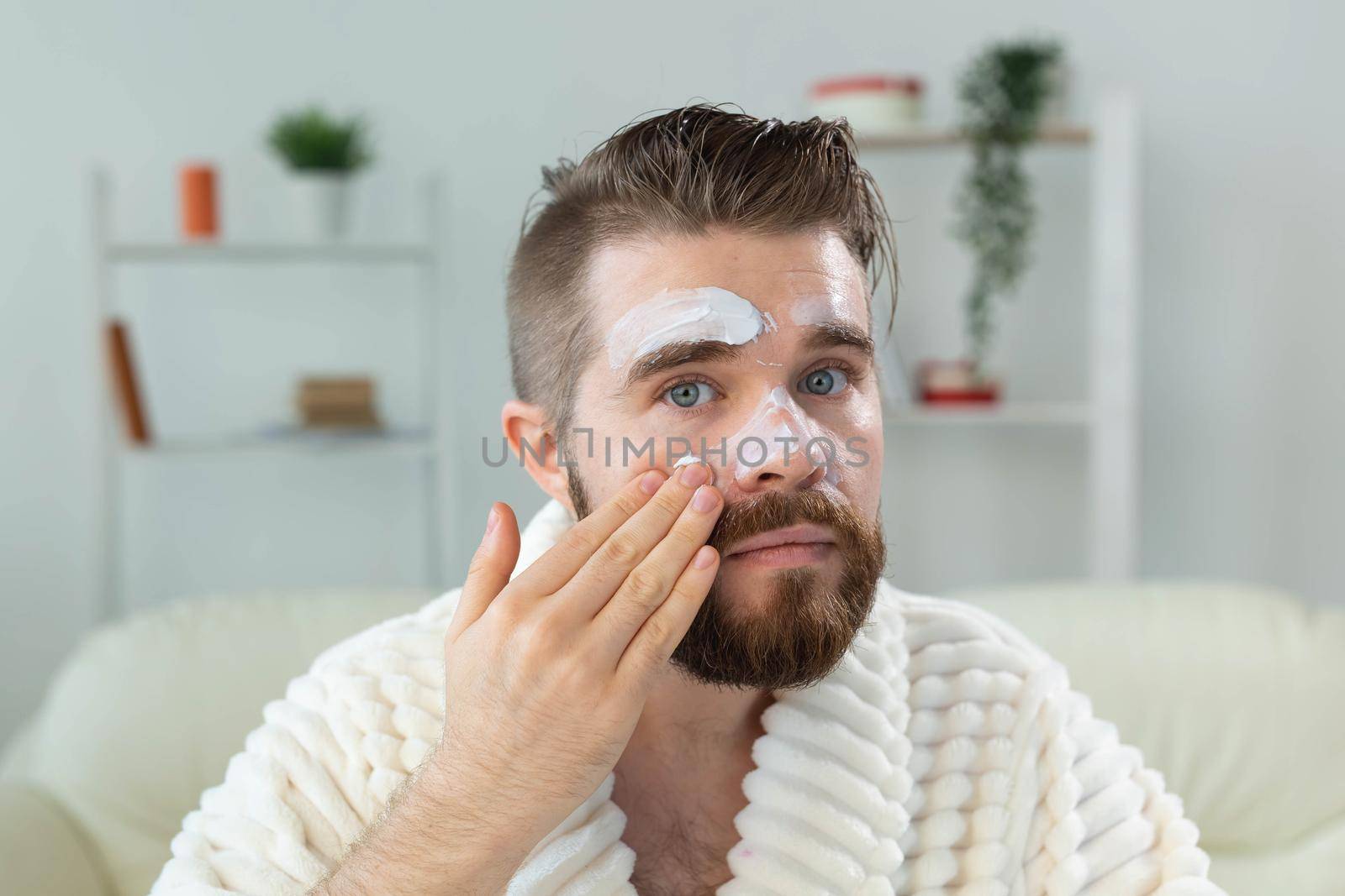 Closeup of handsome young man applying facial cream in front of mirror