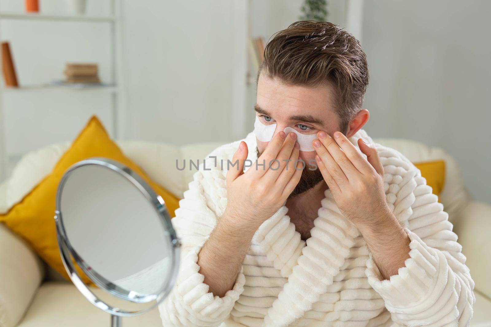 Bearded man applying eye patches on his face. Wrinkles and face home care for men