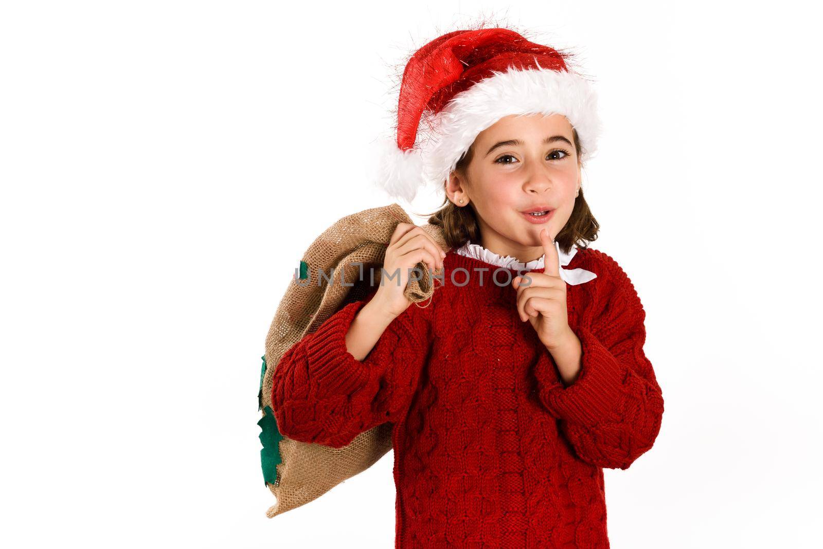 Adorable little girl wearing santa hat carrying gift bag isolated on white background. Winter clothes for Christmas