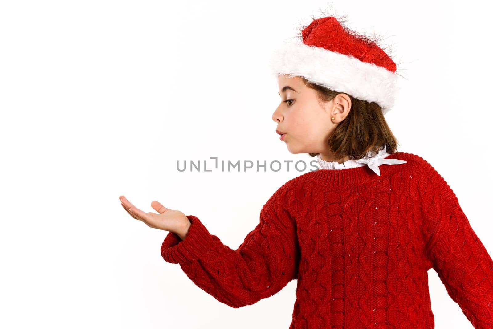 Adorable little girl wearing santa hat blowing to her hand on white background. Winter clothes