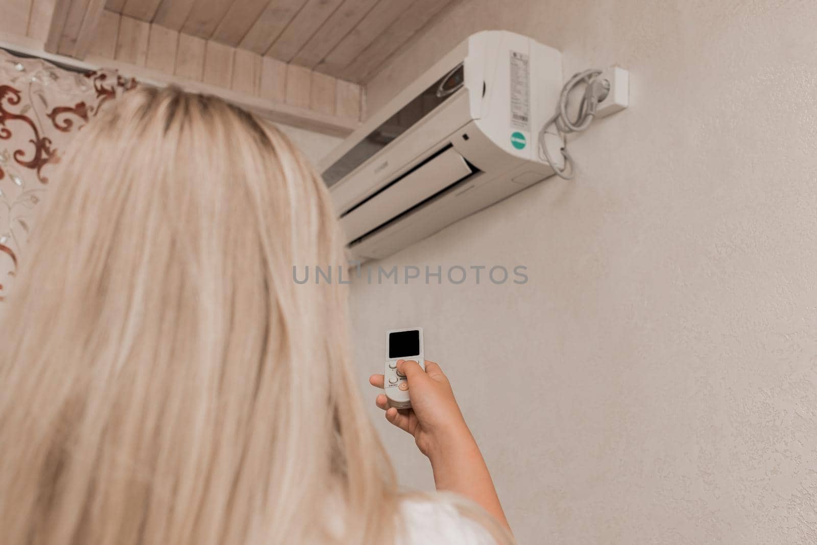 Young girl blonde holds in his hands a remote control of air conditioning in the interior of the room.