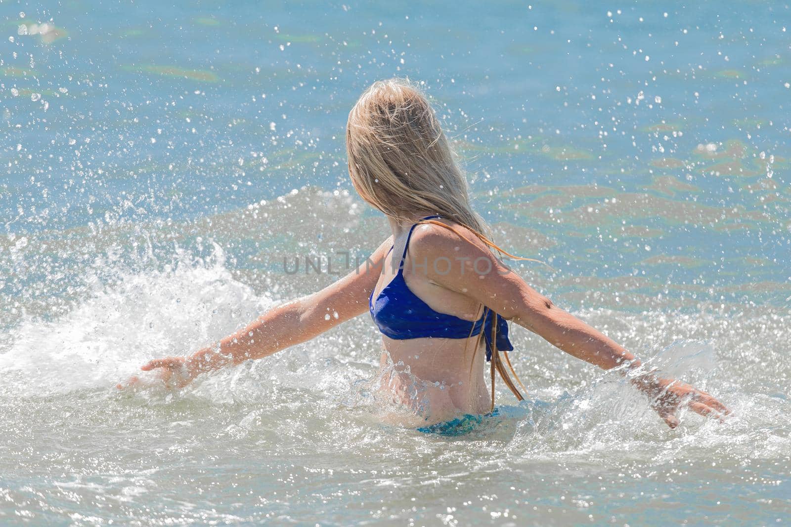 Young cheerful girl teenager blonde makes splashes of water with her hands in the sea.
