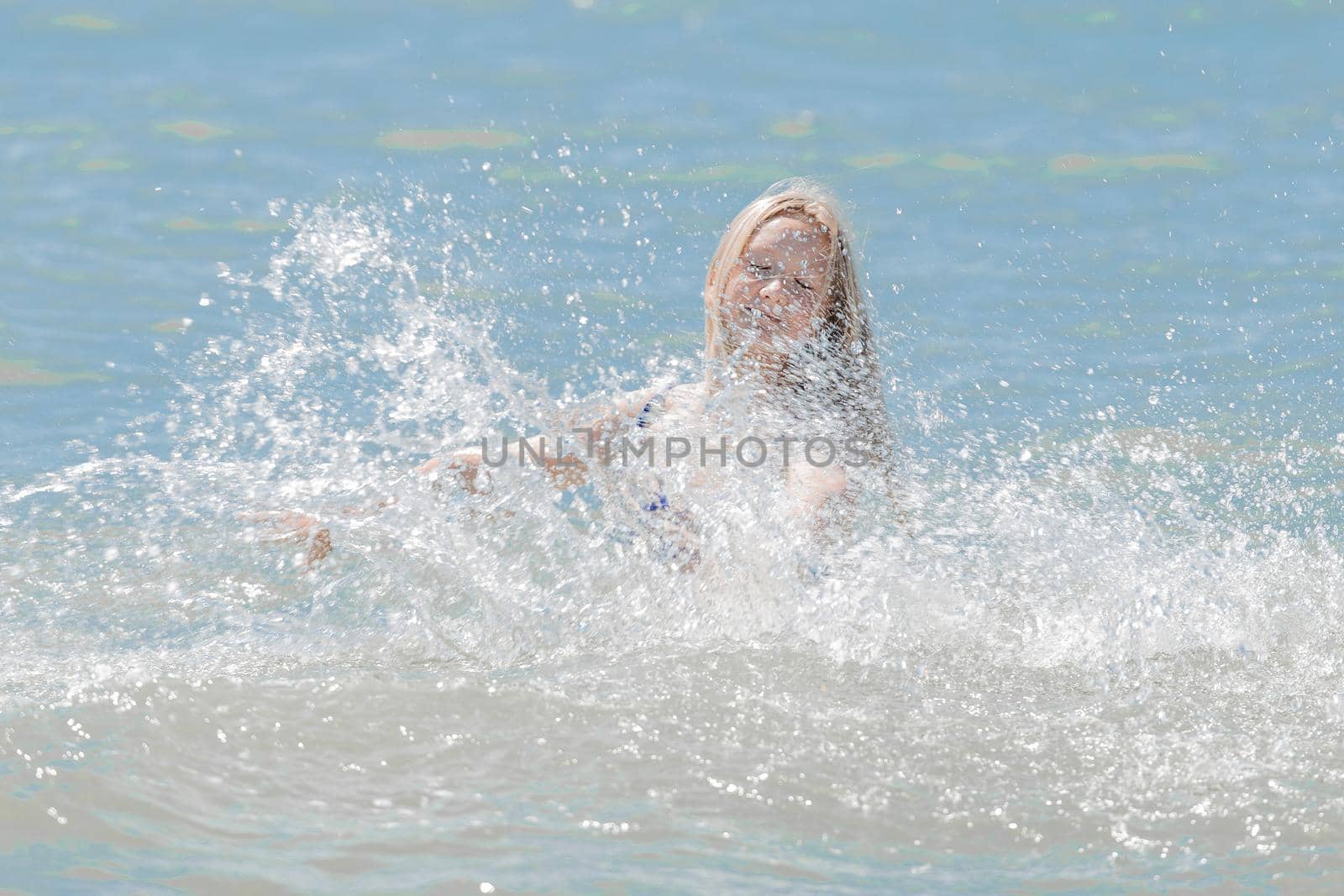 Young cheerful girl teenager blonde European appearance makes splashes of water with her hands in the sea.