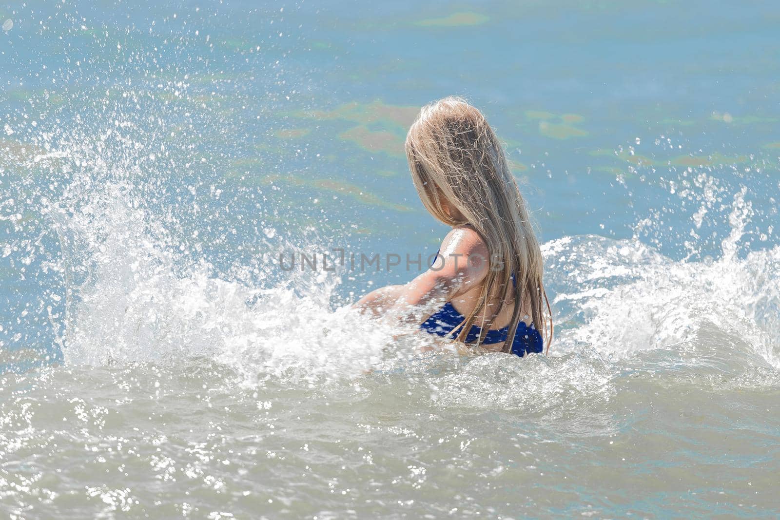 Young cheerful girl teenager blonde makes splashes of water with her hands in the sea.