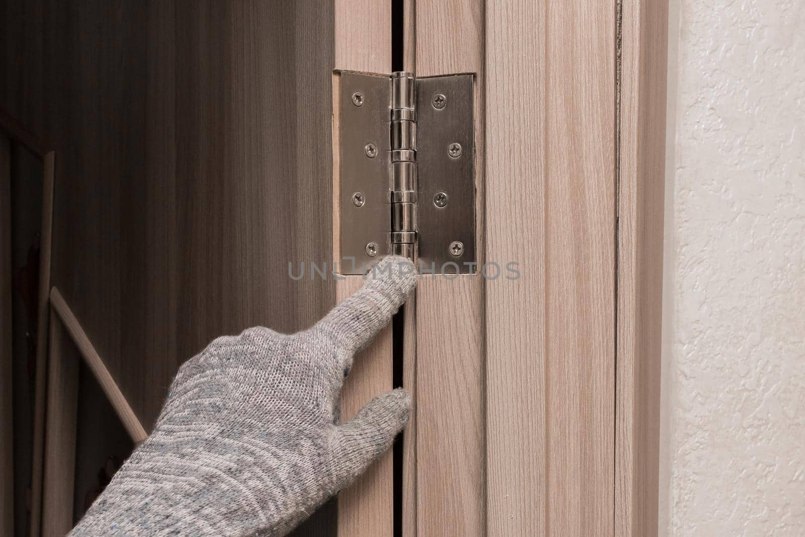 The hand of a man worker in a construction glove points his finger at a wooden door opening with a door iron hinge by AYDO8