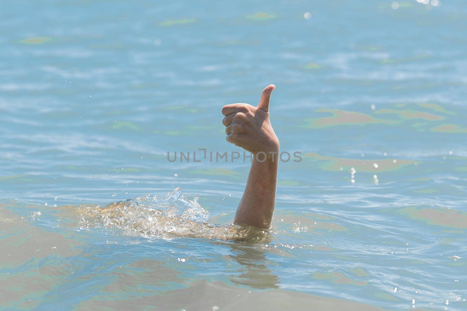 Hand from under the water of a drowning girl shows class with a thumb up. Help and urgent rescue of a person during a dangerous swimming, sos by AYDO8