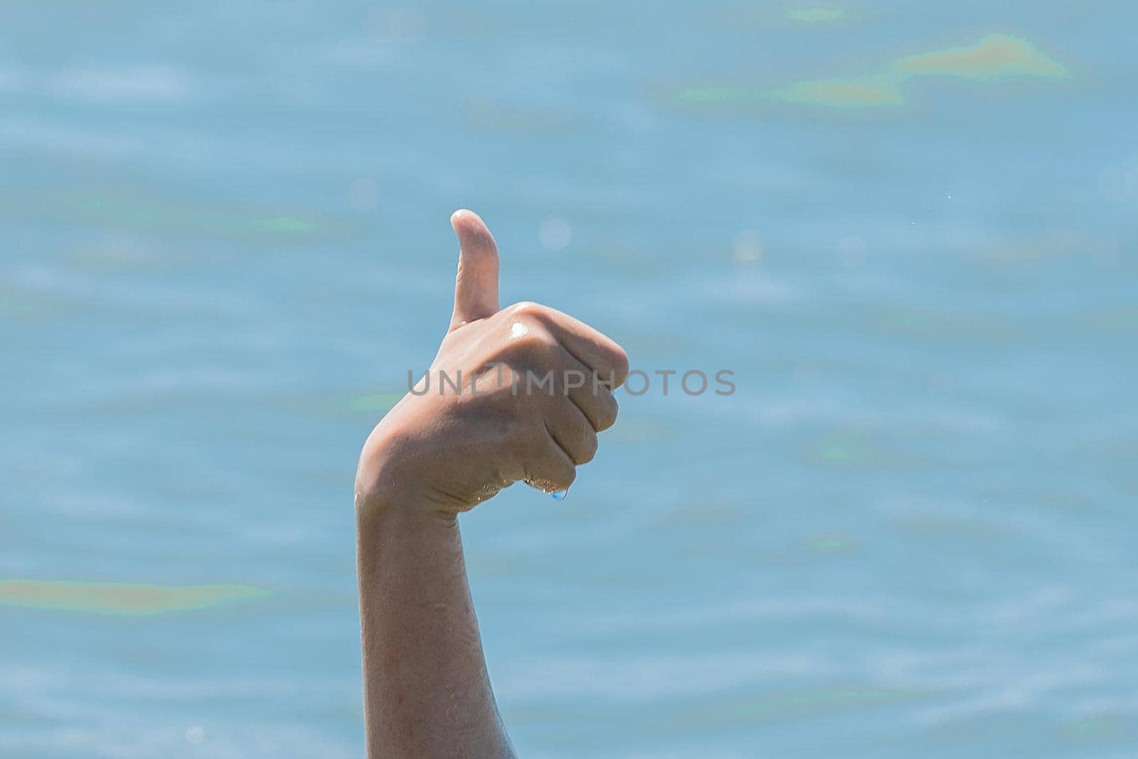 Hand from under the water of a drowning girl shows class with a thumb up. Help and urgent rescue of a person during a dangerous swimming, sos.