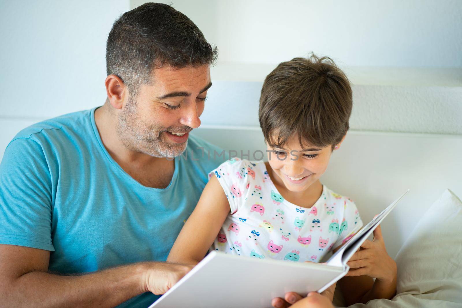 Middle-age father with her eight years daughter using digital tablet in bedroom. Funny dad and lovely little girl are having fun on the bed.