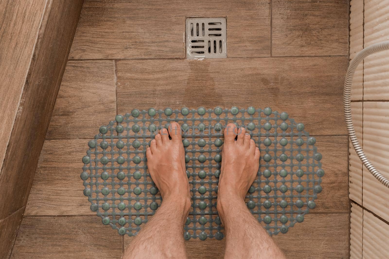 Men's feet stand on a plastic anti-slip mat next to the floor drain in the bathroom or shower by AYDO8