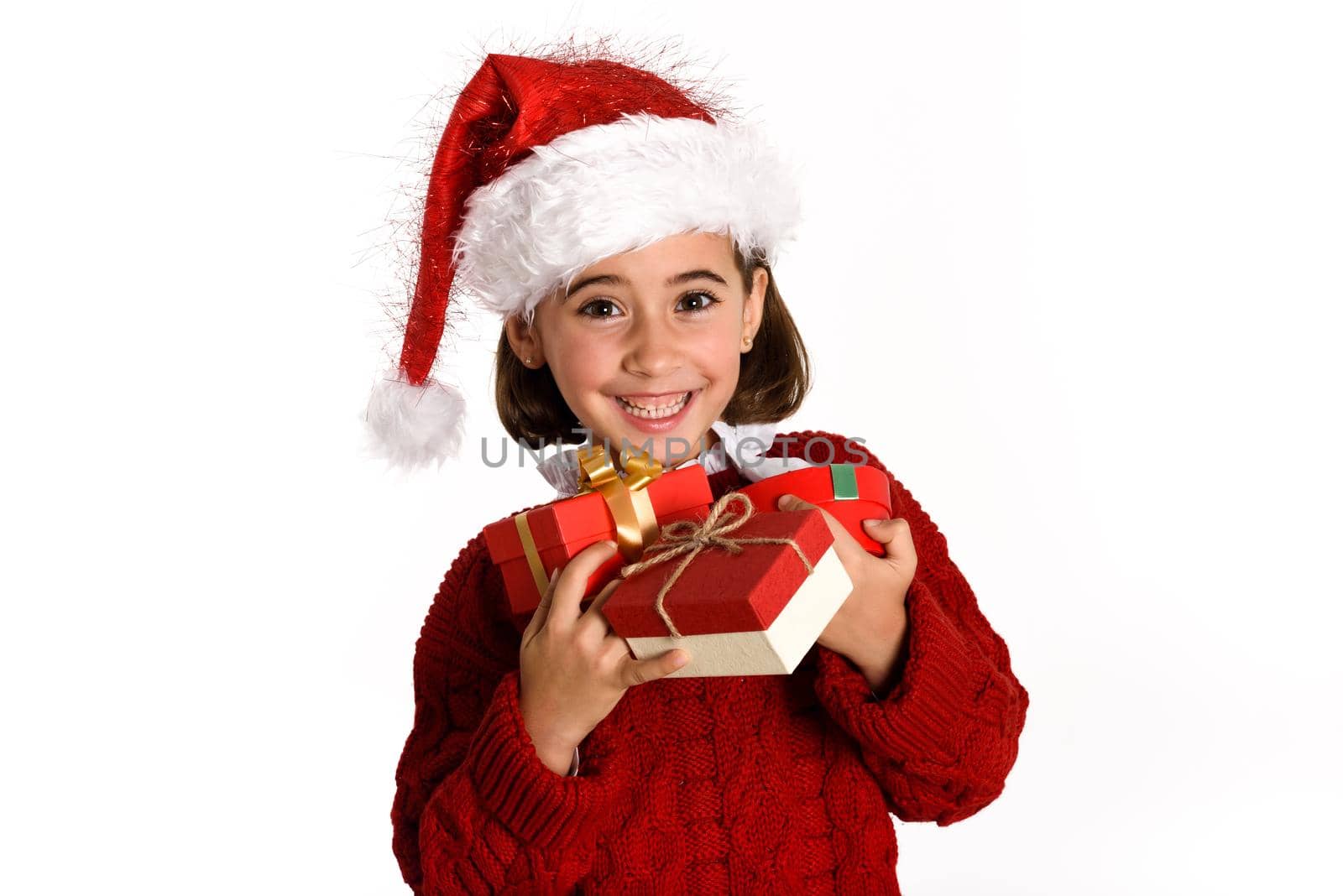 Little girl wearing santa hat carrying many gift boxes for Christmas on white background