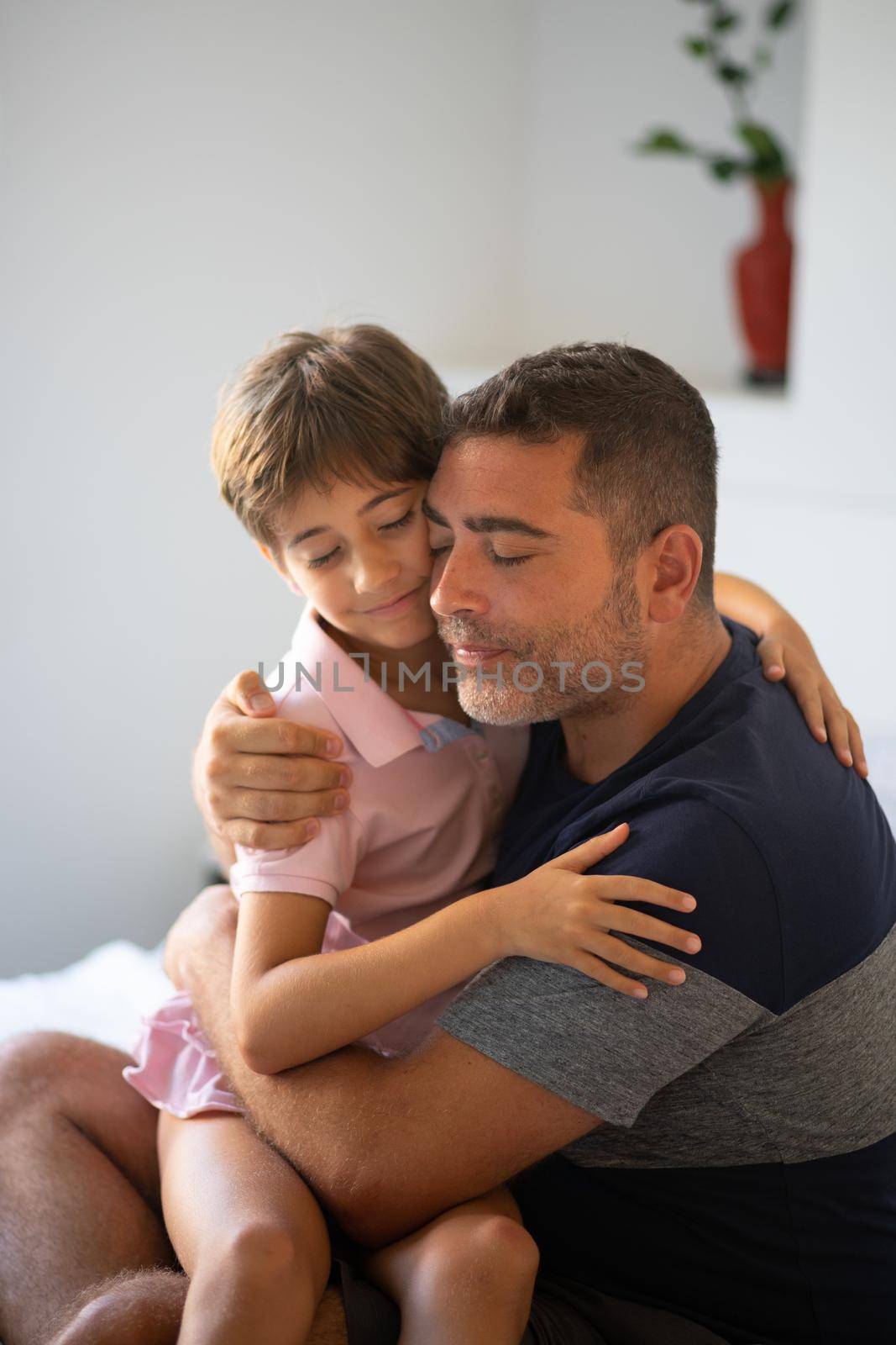 Middle-age father and her little daughter are hugging on the bed. Man spending free time with her daughter.