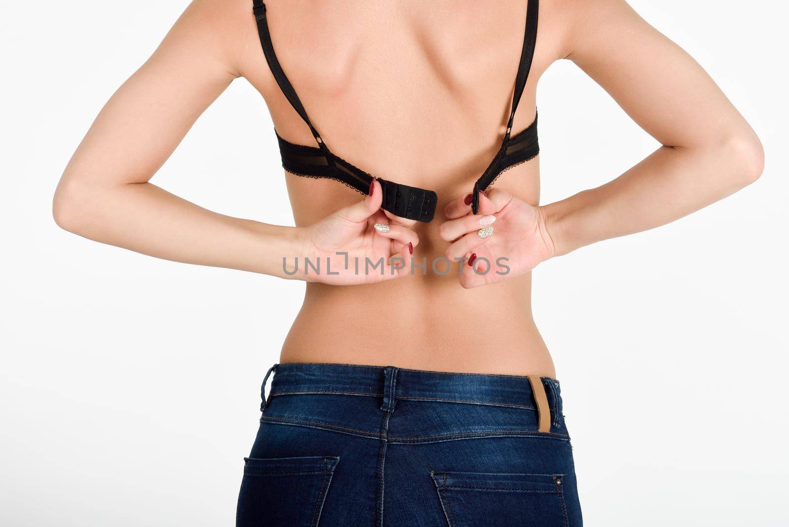 Closeup back view of a woman unhooking the clasp of her black bra. Female wearing blue jeans