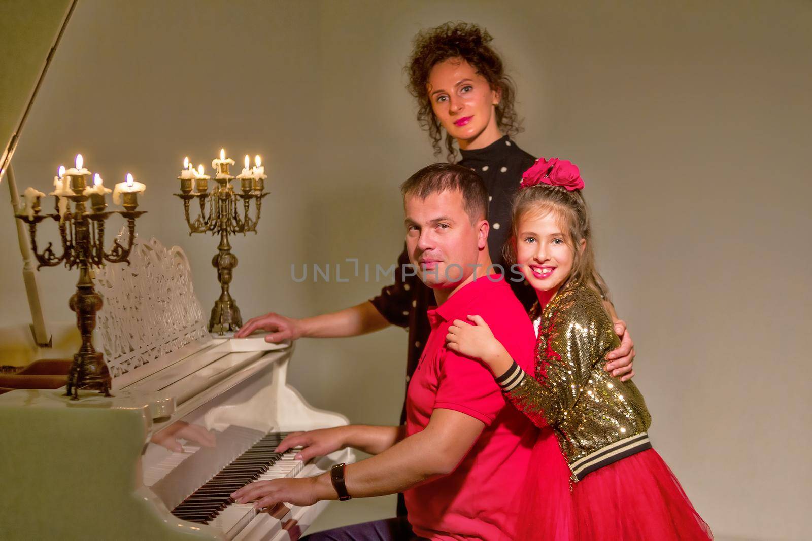 Family on Christmas Eve near an old white piano on which candles by kolesnikov_studio
