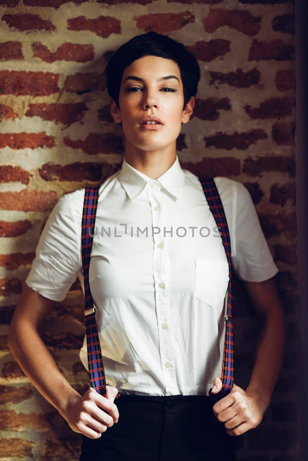 Beautiful young woman, model of fashion, with very short haircut, looking at camera with a brick wall in the background. Beauty and hairstyles concept.