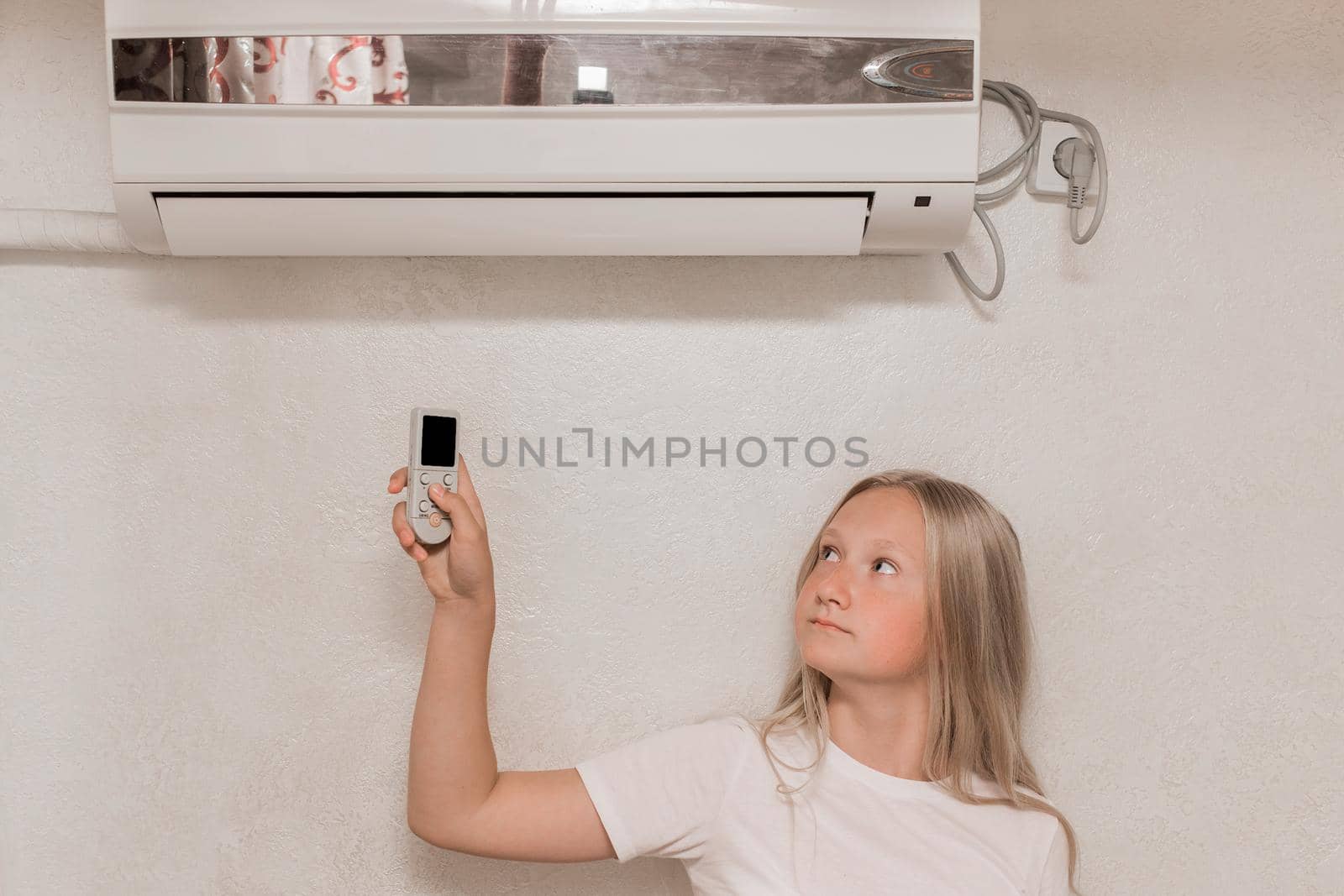 Young girl cute blonde teenager of European appearance holds in his hands a remote control of air conditioning in the interior of the room.