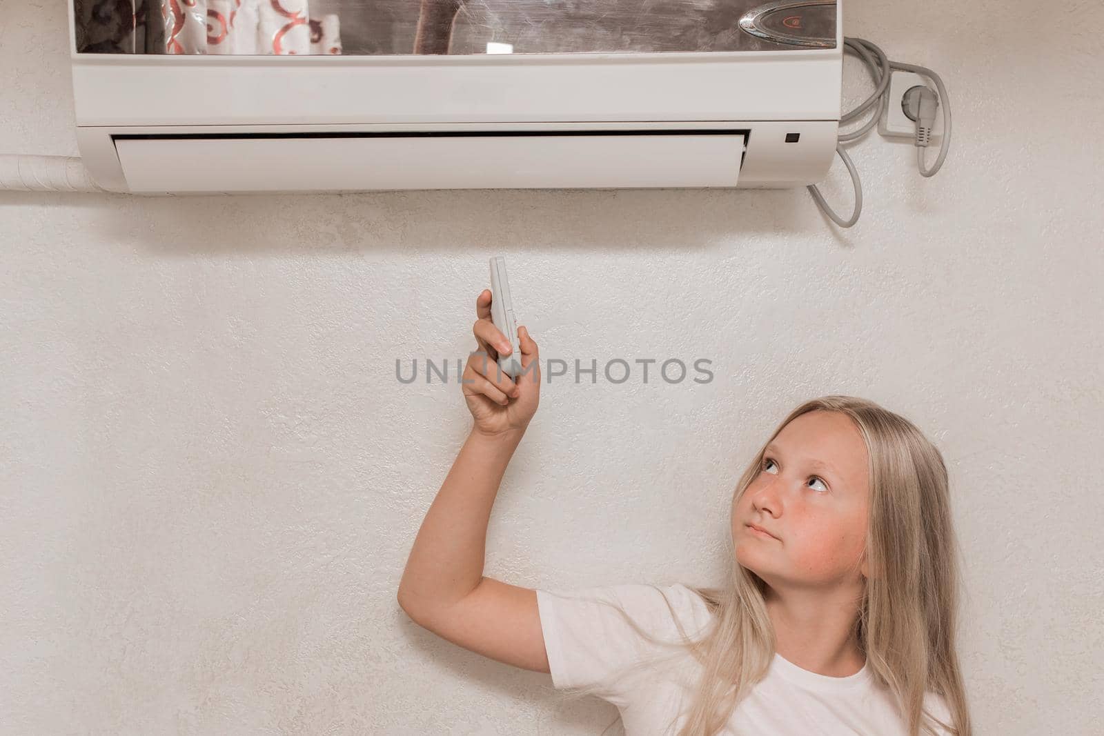 Young girl cute blonde teenager of European appearance holds in his hands a remote control of air conditioning in the interior of the room by AYDO8