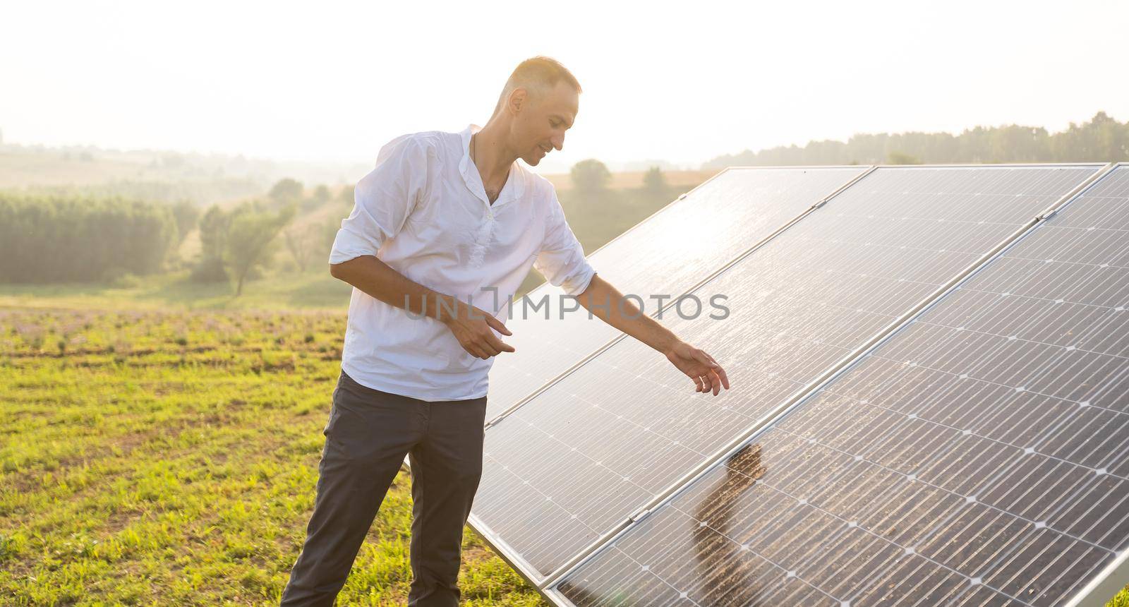 oung engineer is checking an operation of sun and cleanliness of photovoltaic solar panels on a sunset. Concept: renewable energy, technology, electricity, service, green, future.