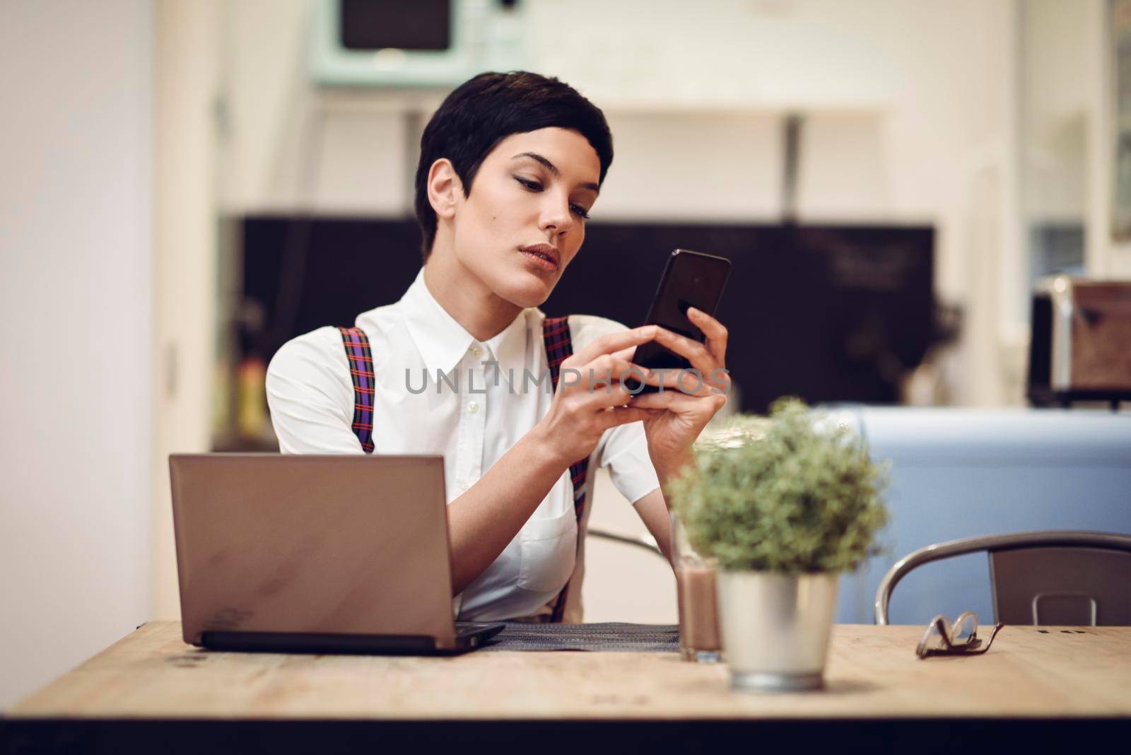 Young woman with very short haircut looking at her smart phone. Businesswoman working at home concept.