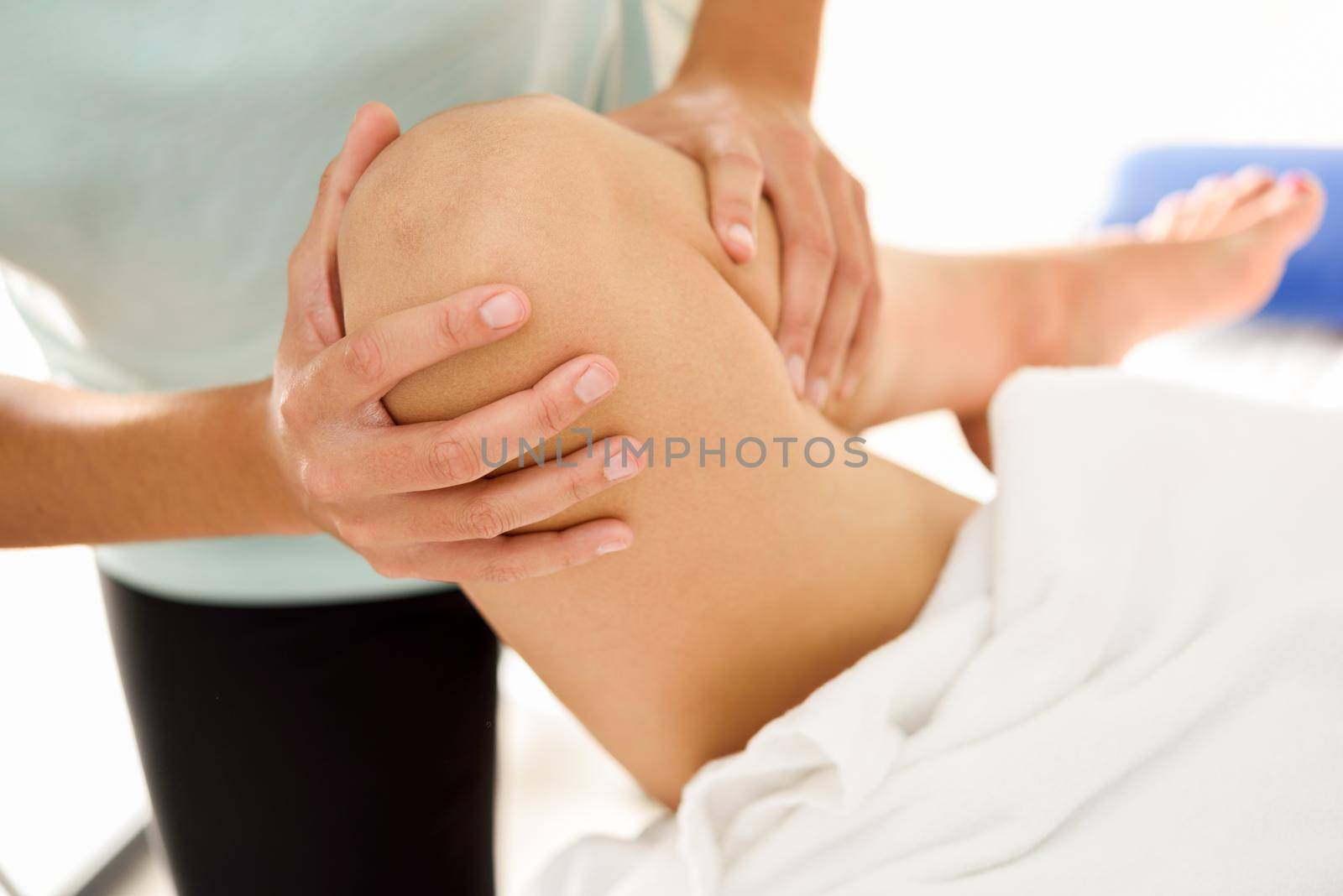 Medical massage at the leg in a physiotherapy center. Female physiotherapist inspecting her patient. Close-up photograph.