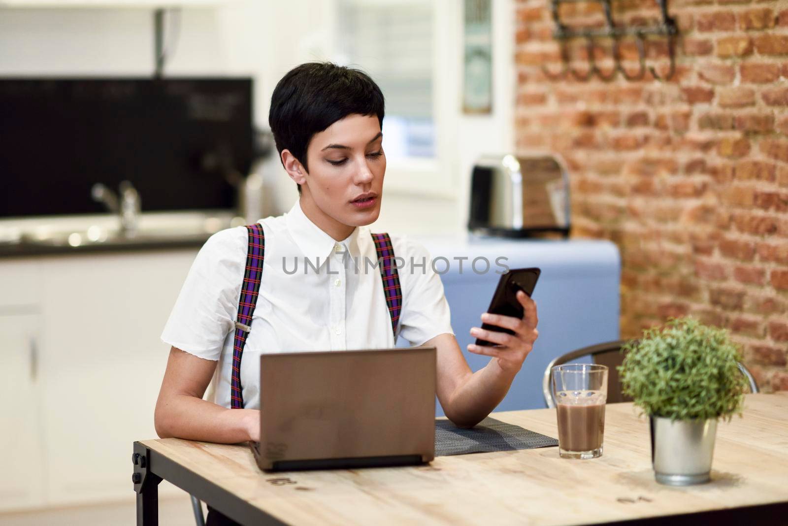 Young woman with very short haircut looking at her smart phone. Businesswoman working at home concept.