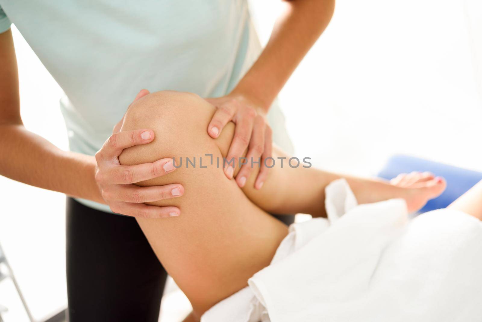 Medical massage at the leg in a physiotherapy center. Female physiotherapist inspecting her patient. Close-up photograph.