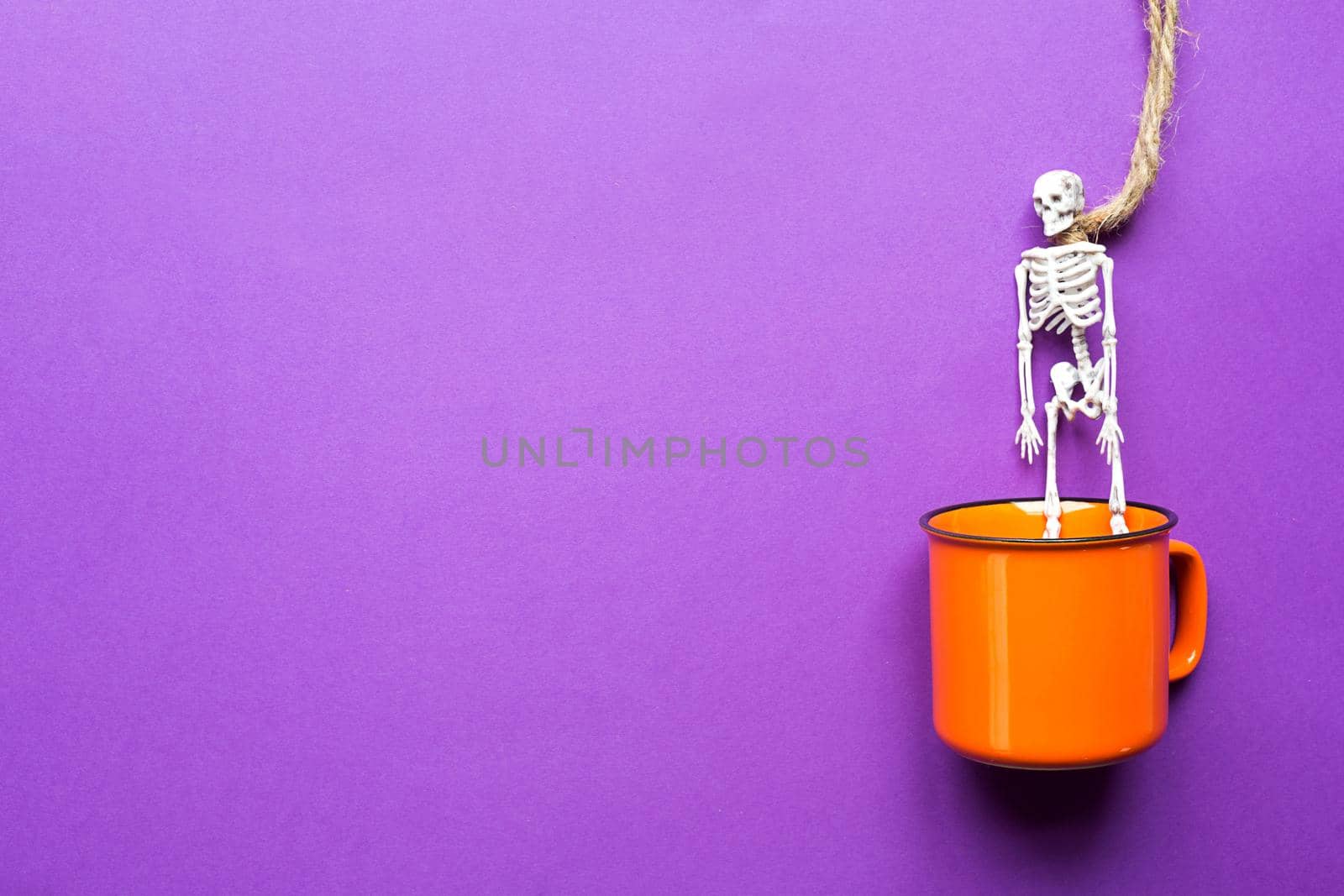 Orange mug on a purple background with terrible Halloween decorations. The concept of the Halloween holiday. Drink, fun, party. Copy space, mock up, flatly