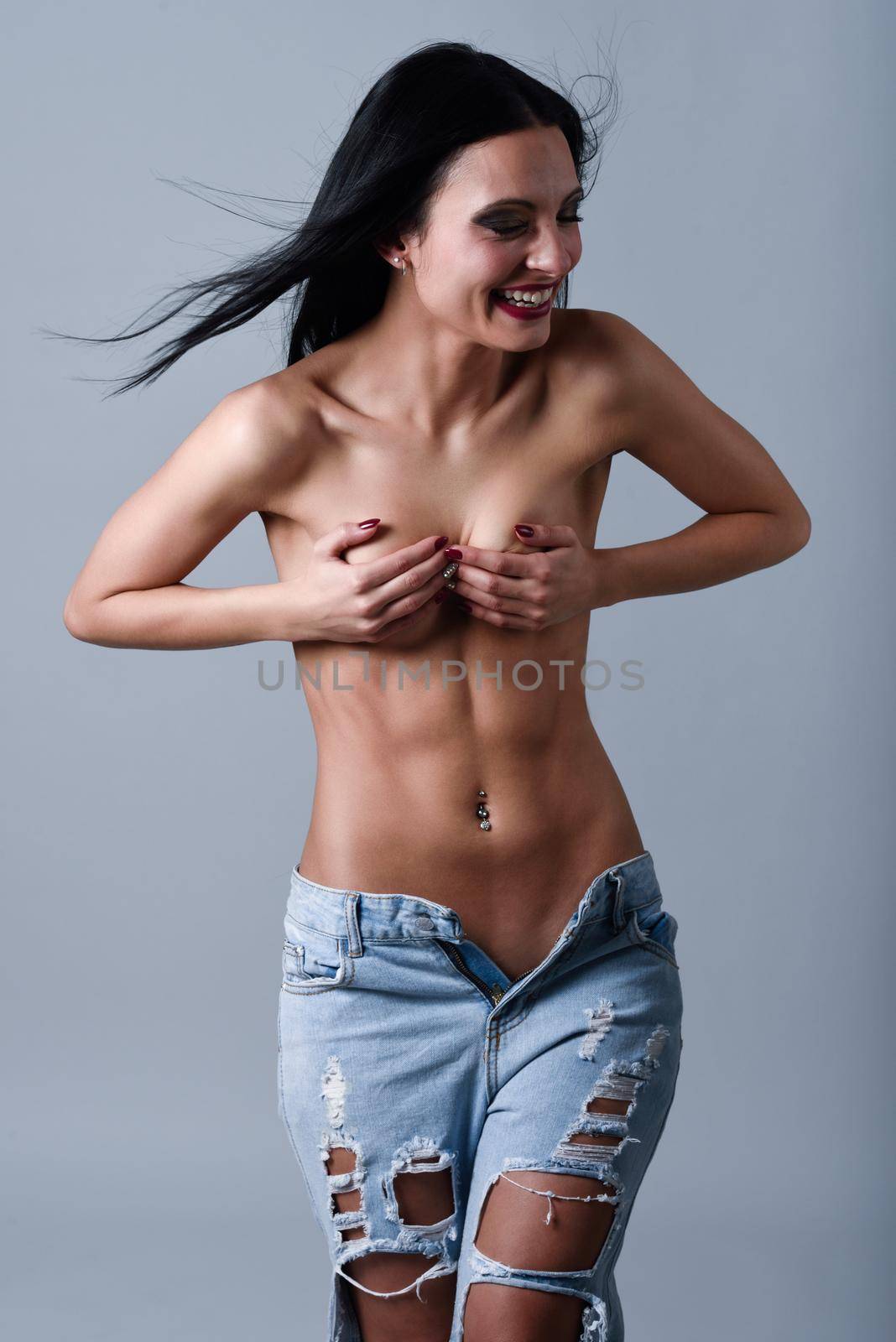 Beautiful young brunette woman wearing broken blue jeans. Beautiful topless girl with moving straight hair laughing. Studio shot.