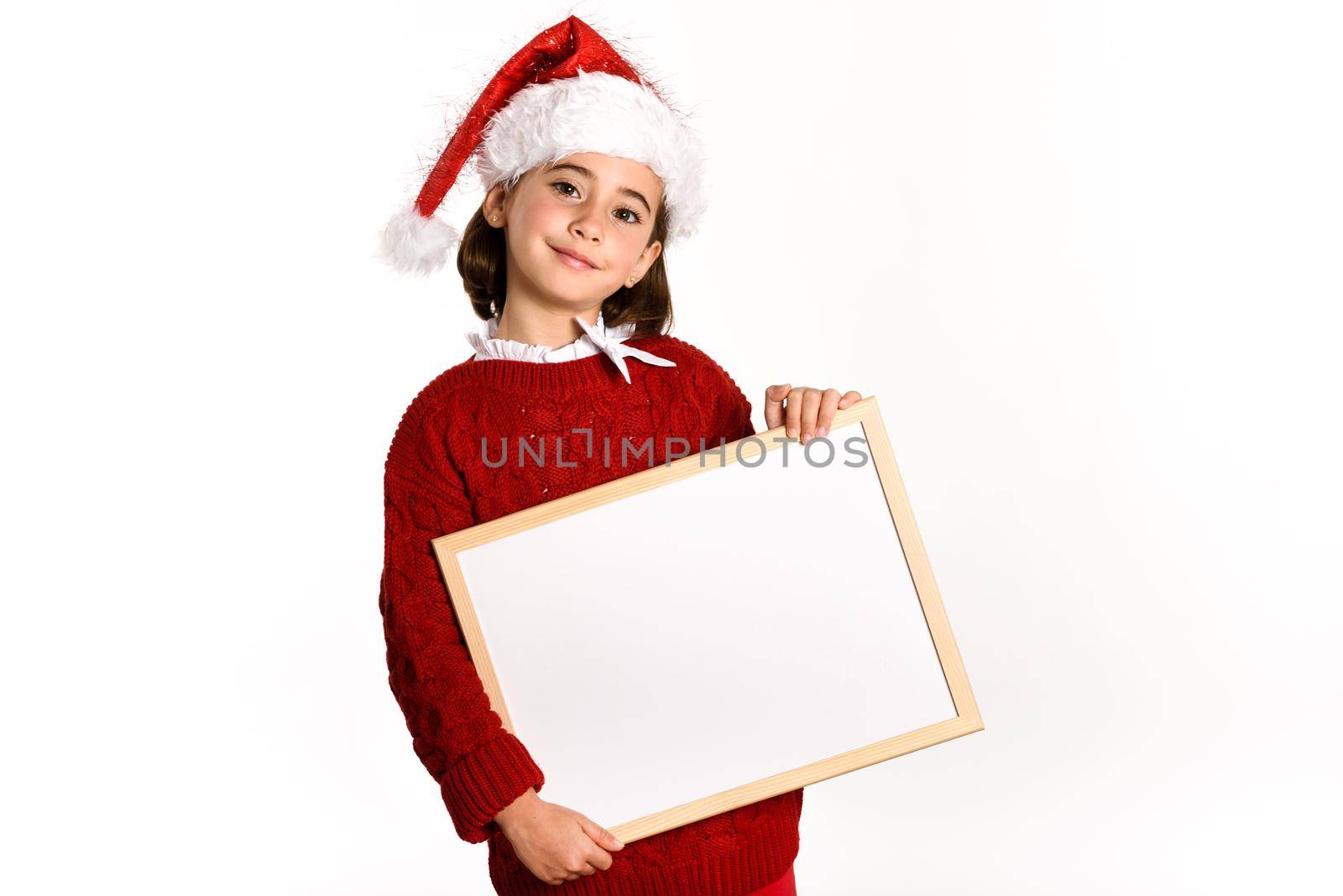 Little girl wearing santa hat holding blank board for advertisementon on white background. Invitation to christmas activities. Winter clothes