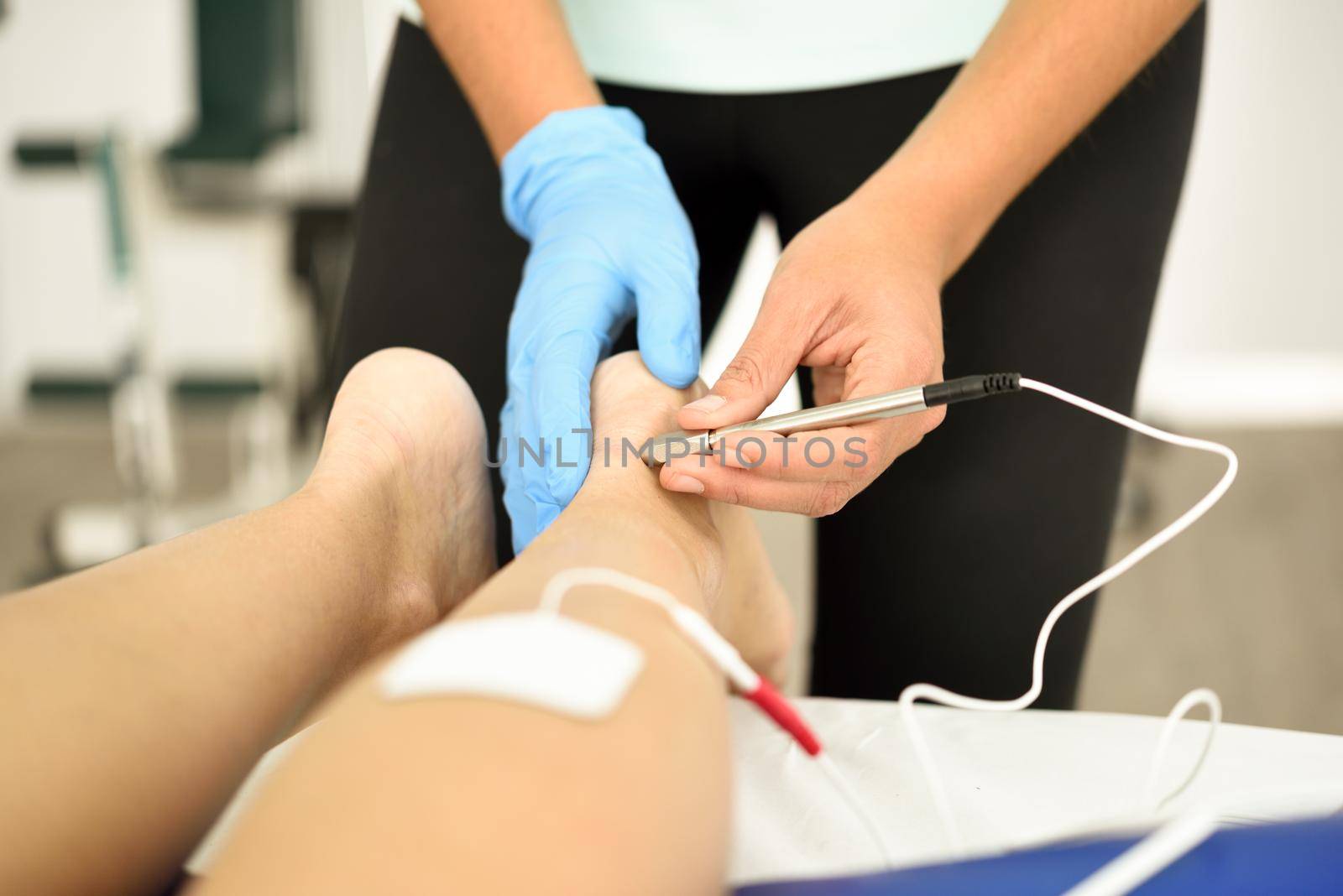 Electroacupuncture dry with needle connecting machine used by acupunturist on female patient for acupuncture guided by EPI Intratissue Percutaneous Electrolisis. Electro stimulation in physical therapy to ankle of a young woman in physiotherapy center.