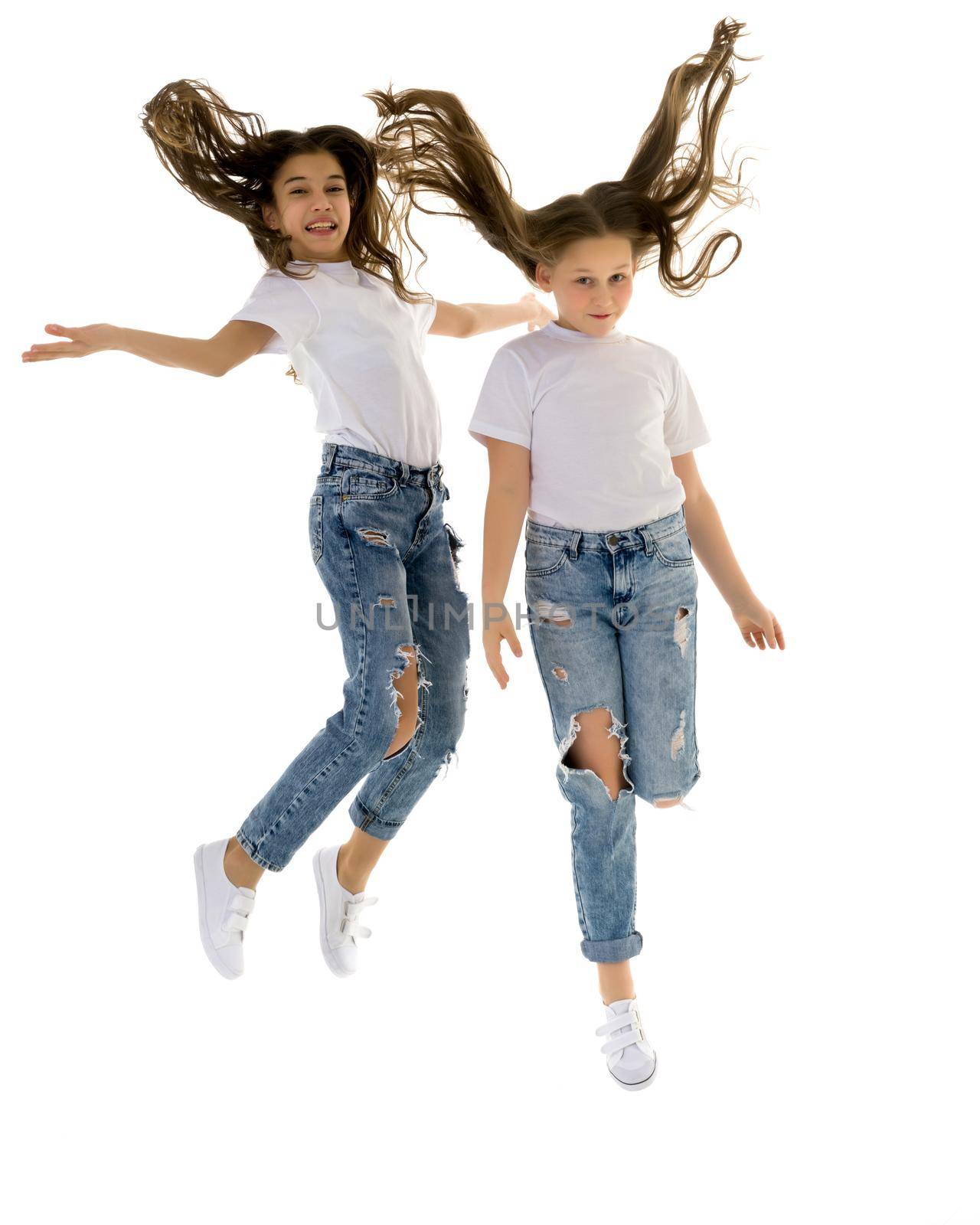 Two cheerful little girls have fun jumping in the studio on a white background.
