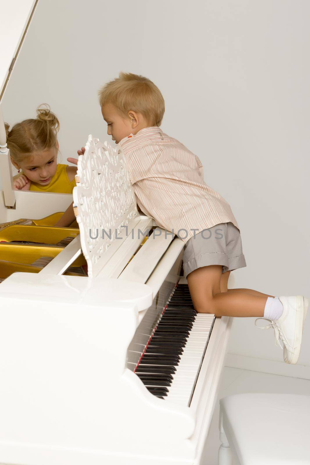 A boy and a girl, brother and sister are studying the device of an old white piano.