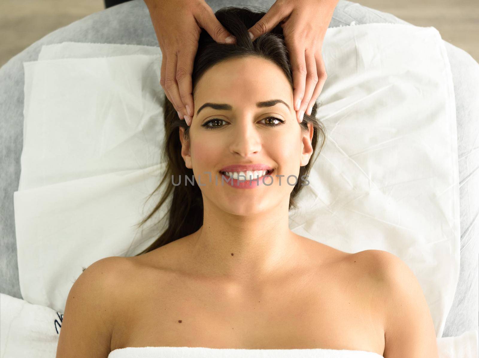 Top view of young caucasian smiling woman receiving a head massage in a spa center. Female patient is receiving treatment by professional therapist.