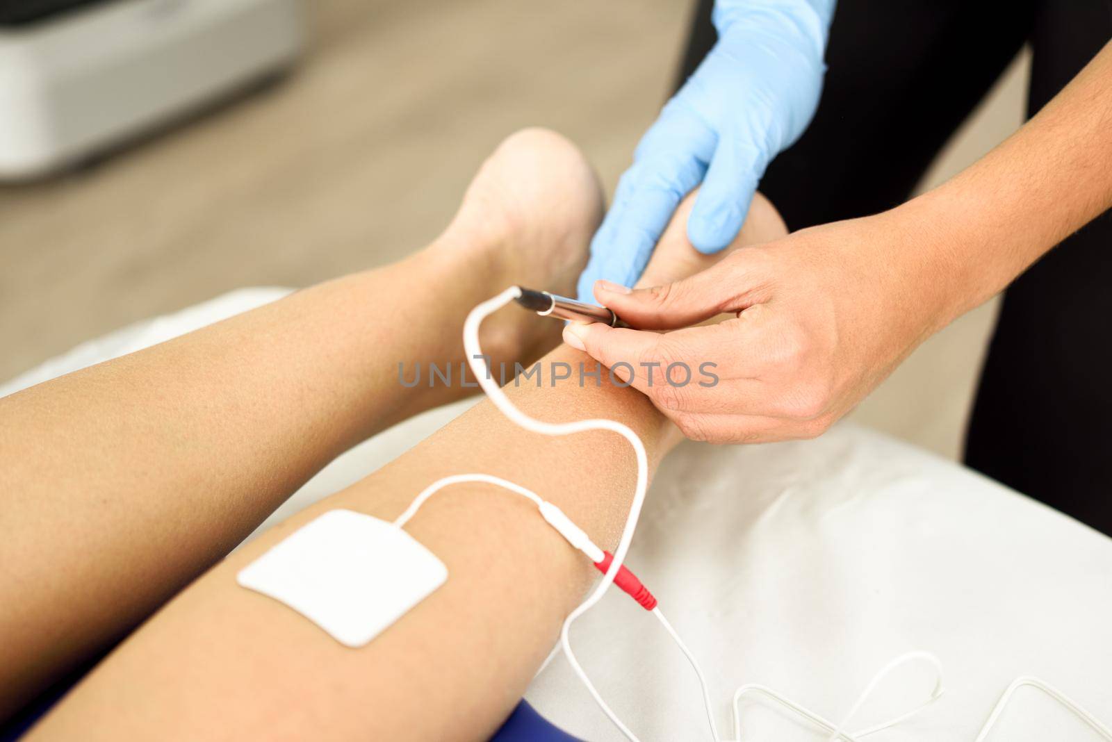 Electroacupuncture dry with needle connecting machine used by acupunturist on female patient for acupuncture guided by EPI Intratissue Percutaneous Electrolisis. Electro stimulation in physical therapy to ankle of a young woman in physiotherapy center.