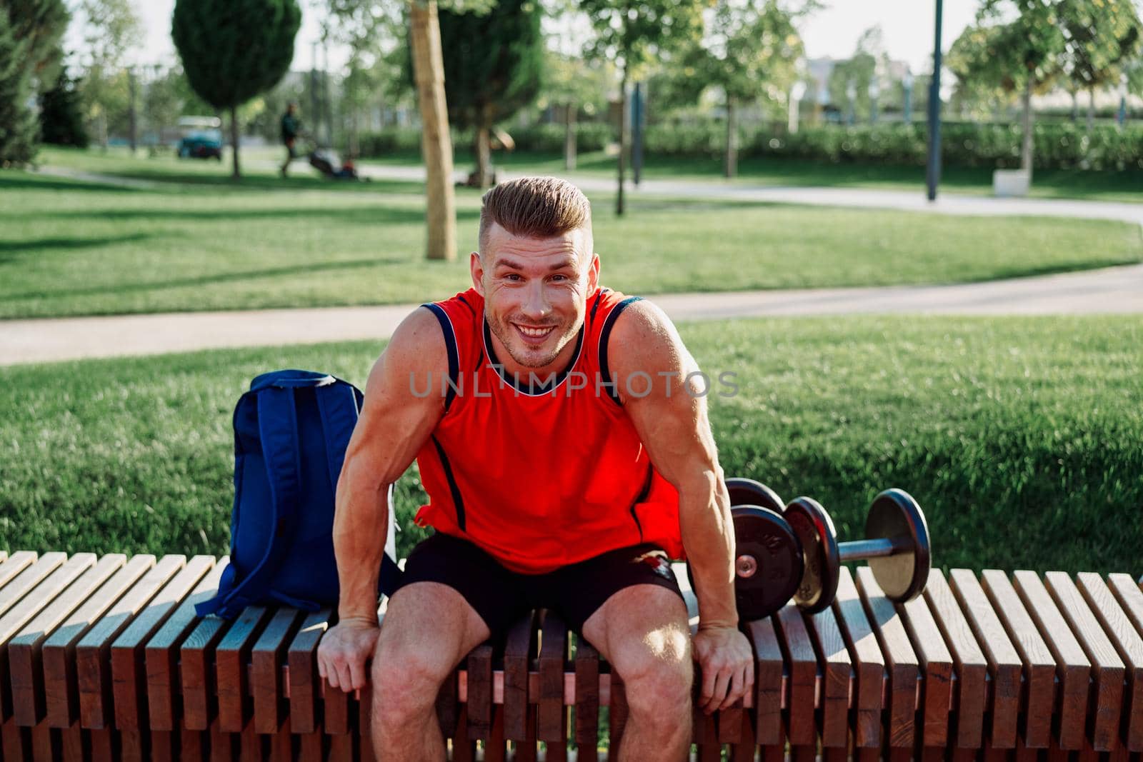 Cheerful male athlete in the park sits on a bench by Vichizh