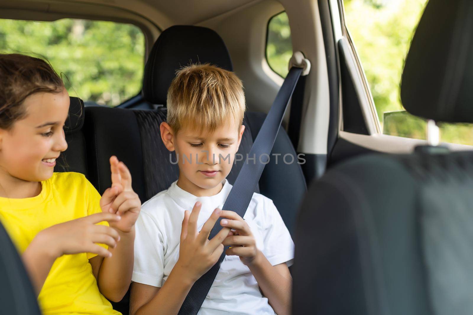 Smiling kids sitting on back seat of car.