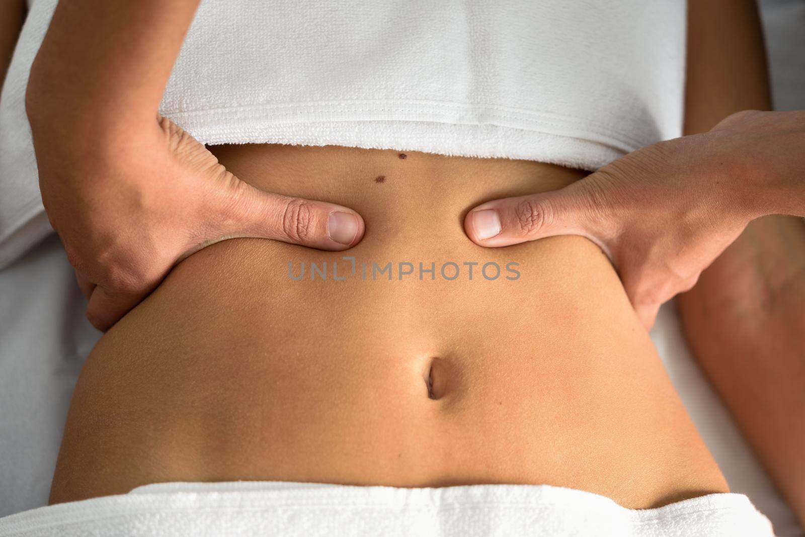 Hands massaging female abdomen.Therapist applying pressure on belly. Woman receiving massage at spa salon