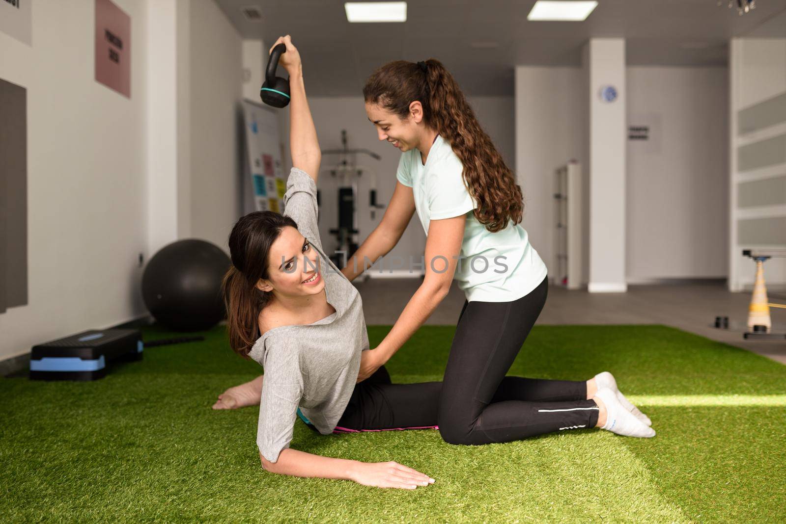 Physical therapist assisting young caucasian woman with exercise with dumbbell during rehabilitation in the gym at hospital. Female physiotherapist training a patient in physiotherapy center.