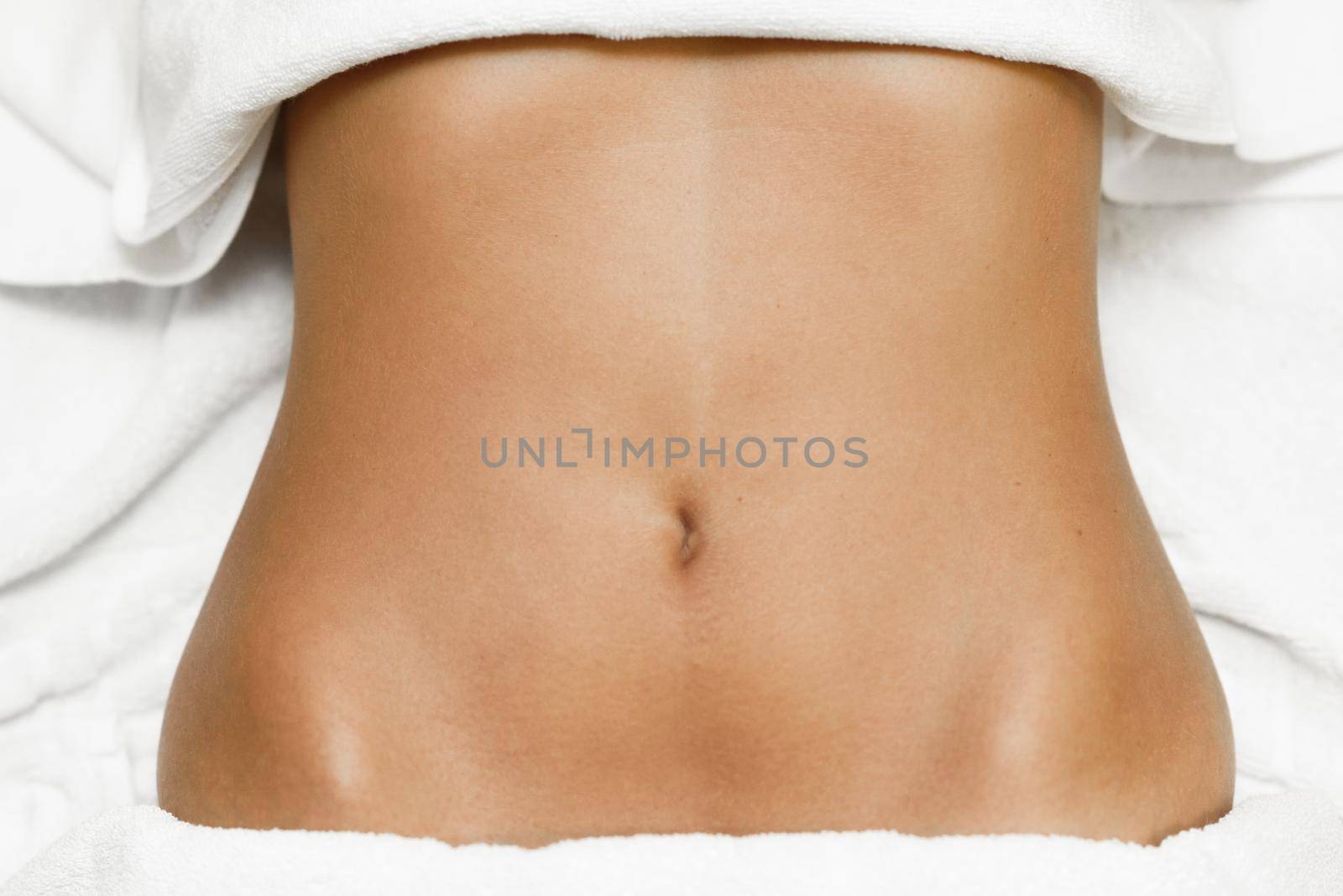 Top view of tan female abdomen laying on spa bed with white towels.