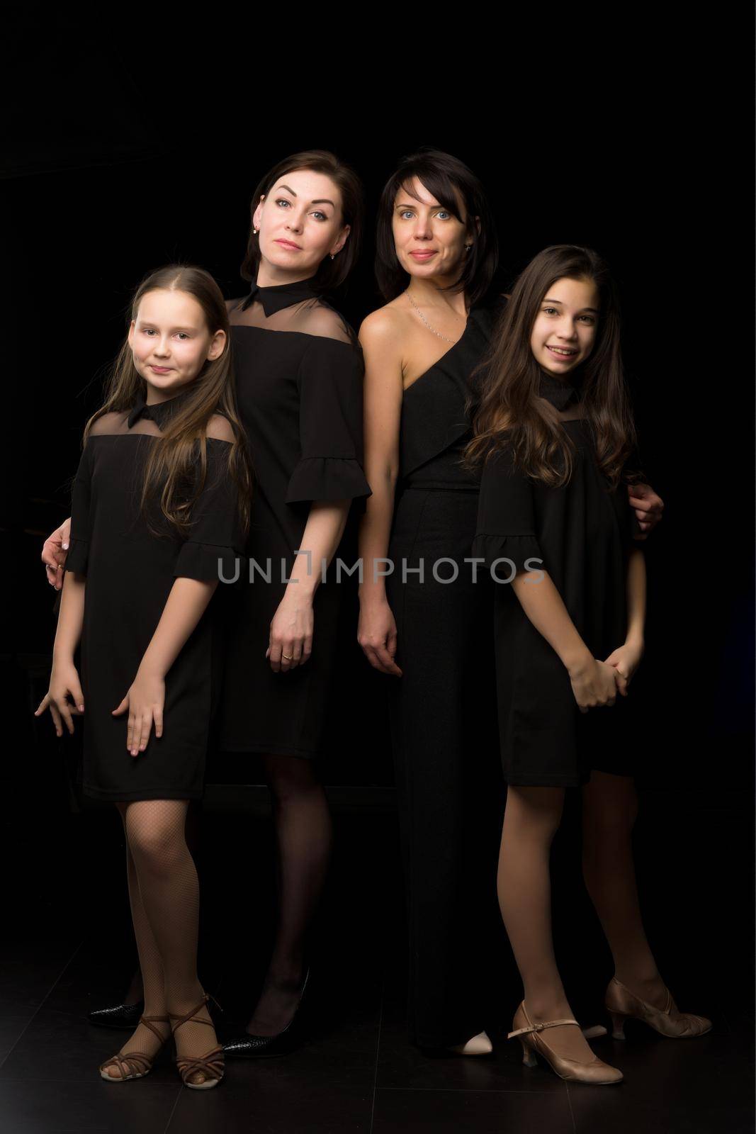 Young, Beautiful mothers with two charming daughters. Studio portrait on a black background. by kolesnikov_studio