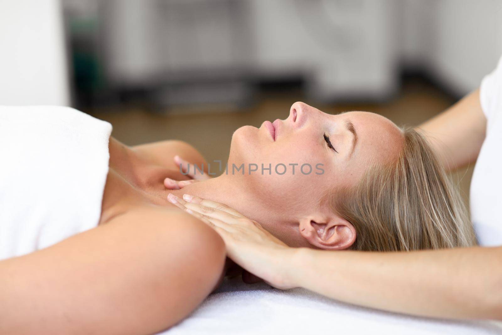 Young blond woman receiving a head massage in a spa center with eyes closed. Female patient is receiving treatment by professional therapist.