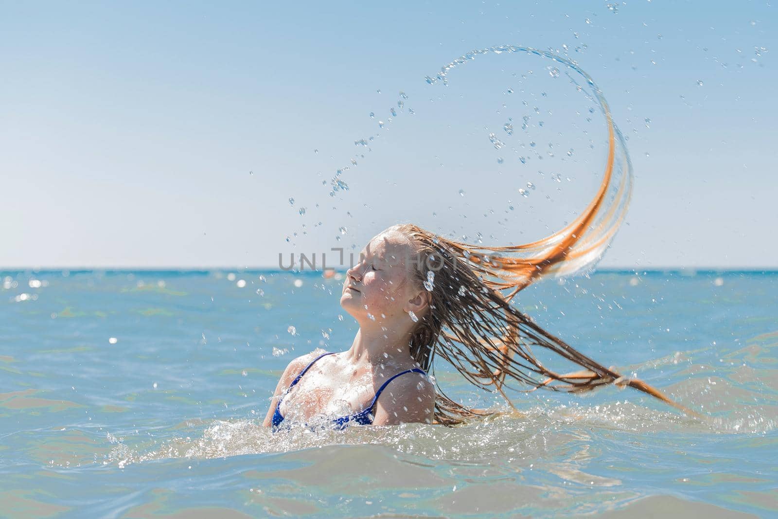 Young attractive girl teenager of European appearance throws wet, long hair up into the sea against the background of the horizon line and blue sky by AYDO8