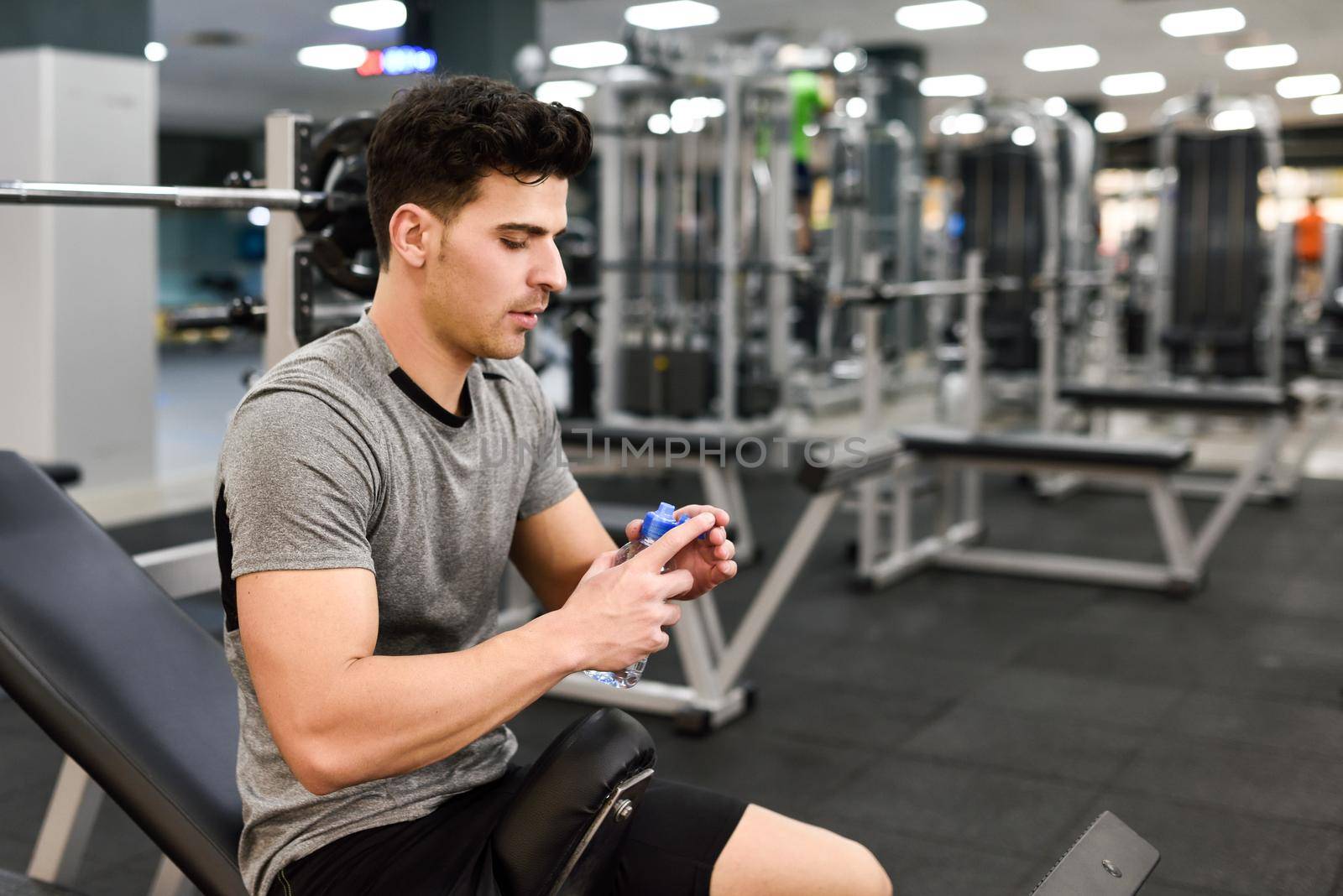 Handsome young man in sportswear holding water bottle at gym by javiindy