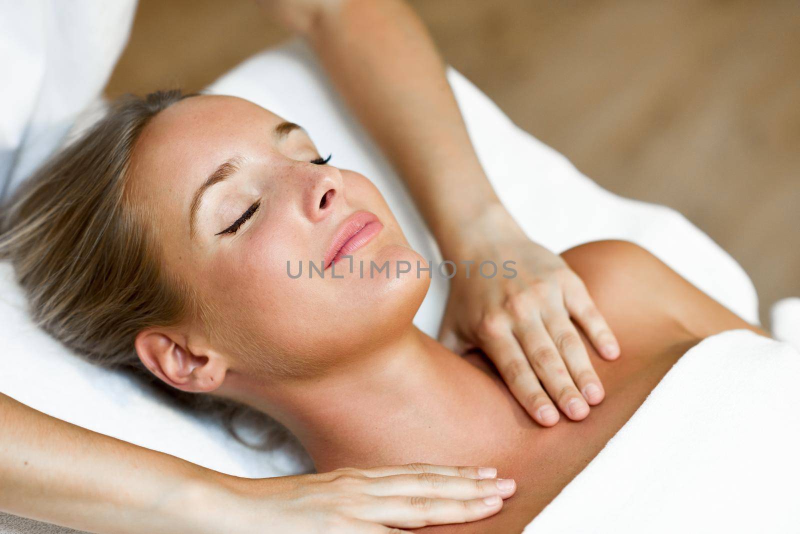Young blond woman receiving a head massage in a spa center with eyes closed and smiling. Female patient is receiving treatment by professional therapist.