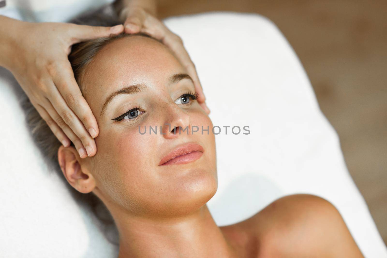 Young blond woman receiving a head massage in a spa center with blue eyes. Female patient is receiving treatment by professional therapist.
