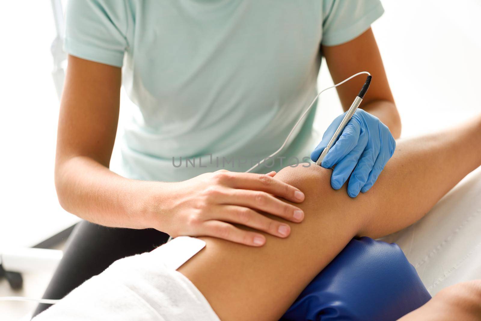 Electroacupuncture dry with needle connecting machine used by acupunturist on female patient for acupuncture guided by EPI Intratissue Percutaneous Electrolisis. Electro stimulation in physical therapy to knee of a young woman in physiotherapy center.
