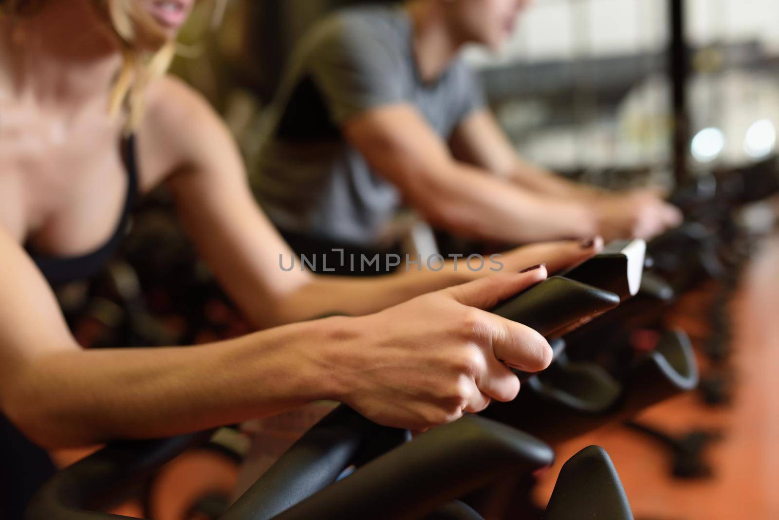 Two people biking in the gym, exercising legs doing cardio workout cycling bikes. Couple in a spinning class wearing sportswear.