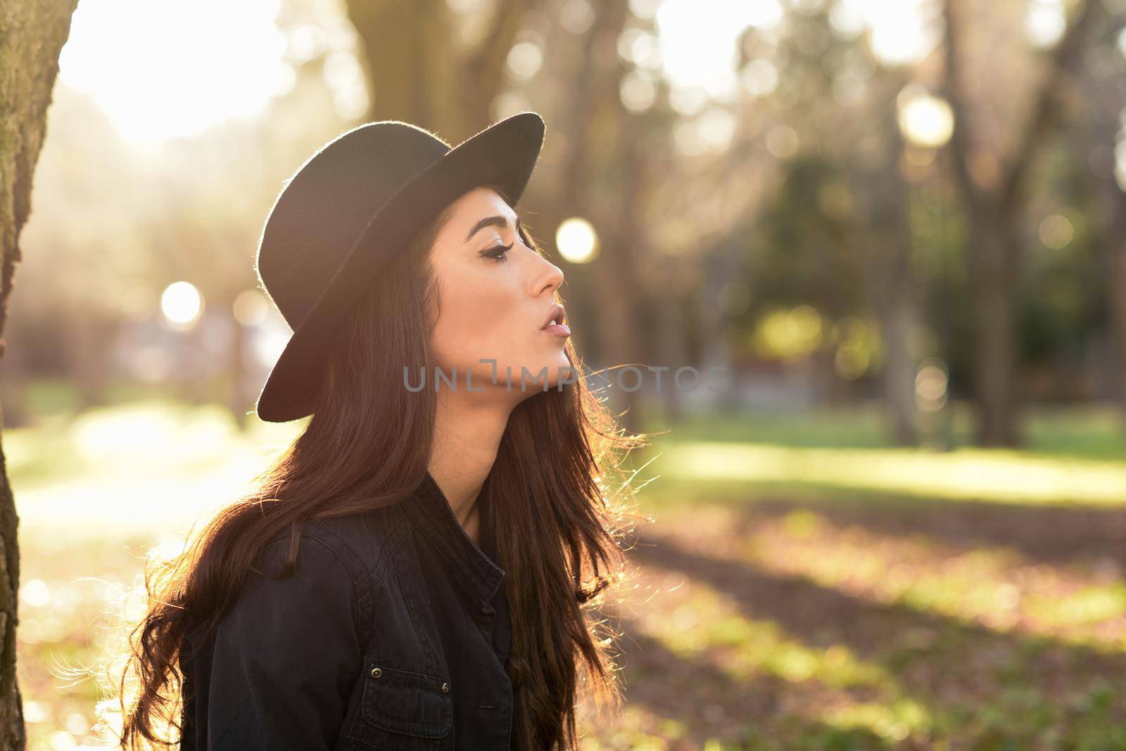 Thoughtful woman sitting alone outdoors wearing hat by javiindy